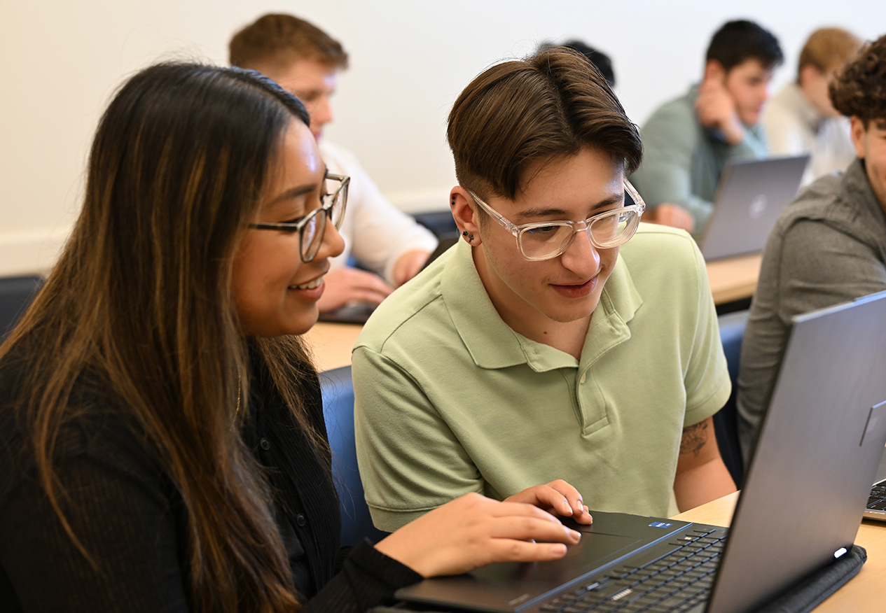 Students working together on a laptop in a classroom.