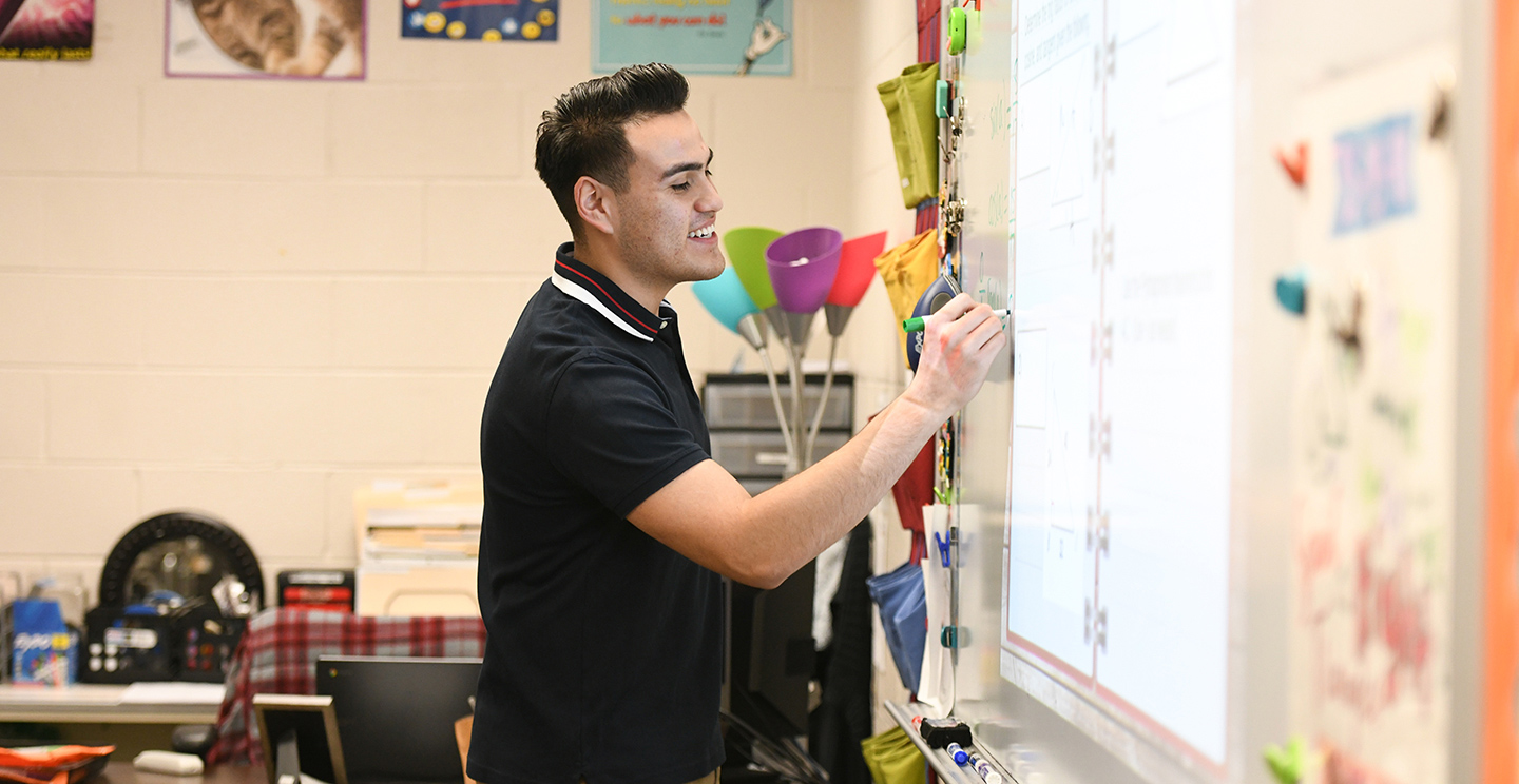 Male teacher writing on a dry erase board.
