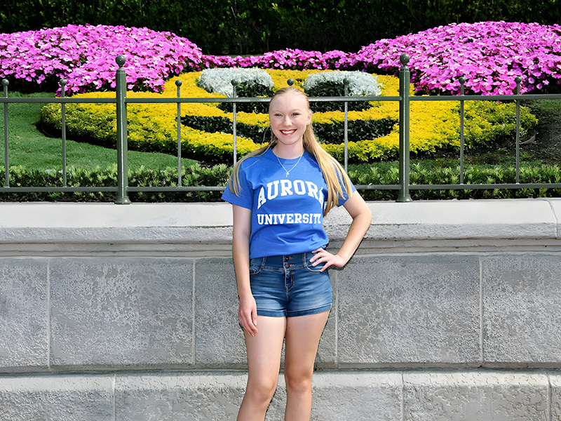 Alayna Nosalik smiles at the camera in front of a Mickey Mouse shaped floral display in Epcot.