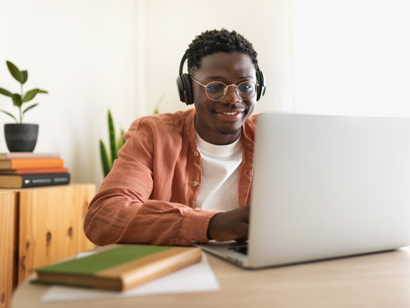 college student smiles while working on a laptop in a bright home-like setting